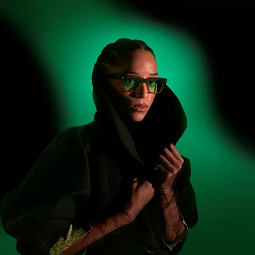 Woman with green tinted sunglasses in front of a dark green background